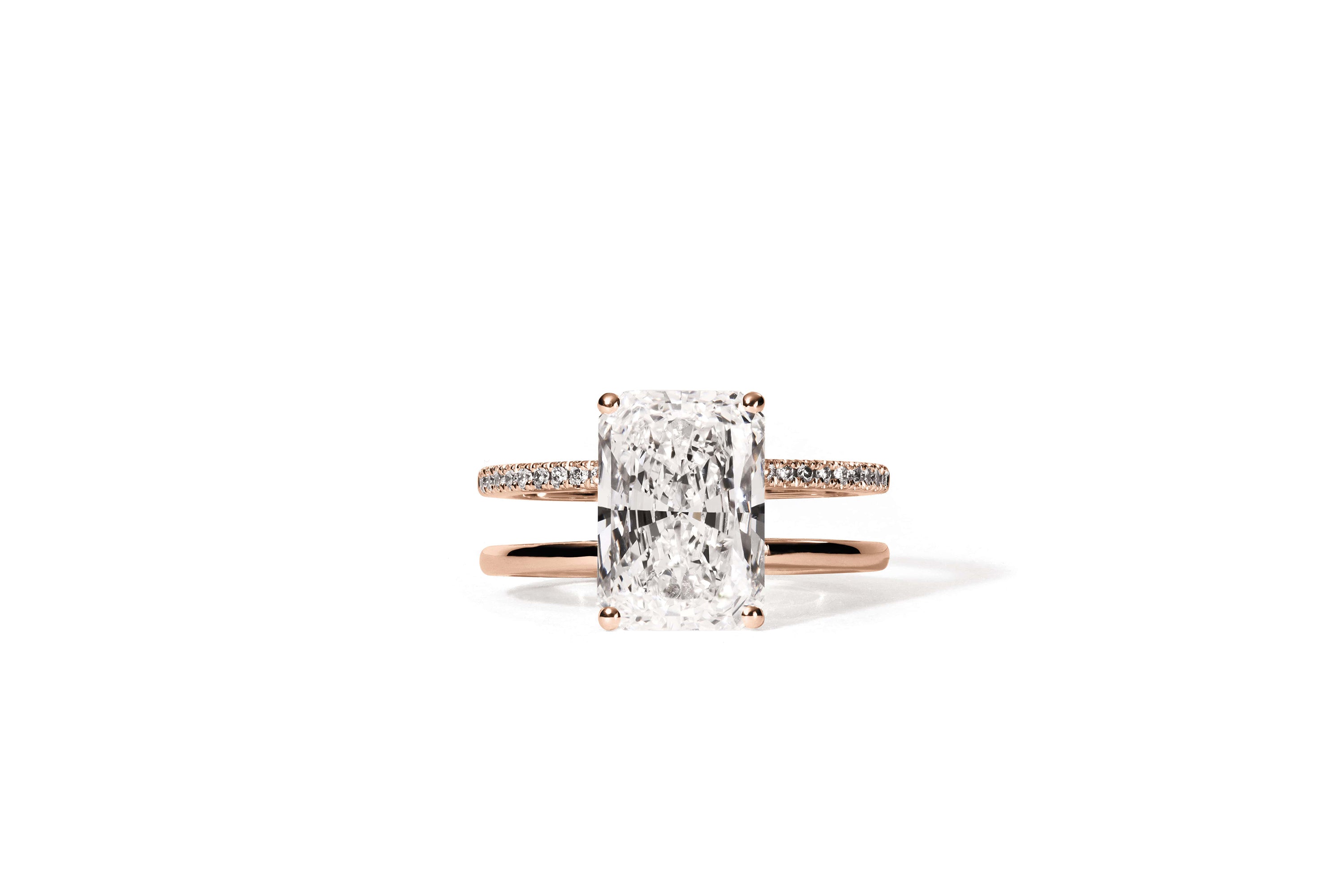 Der Ring APHRODITE ROSÉGOLD von Atelier Sofia besticht in seiner Mitte durch einen Diamanten im Radiantschliff, der durch kleinere, im Labor gezüchtete Diamanten auf der Ringschiene akzentuiert wird und sich elegant auf einem schlichten weißen Hintergrund abhebt.