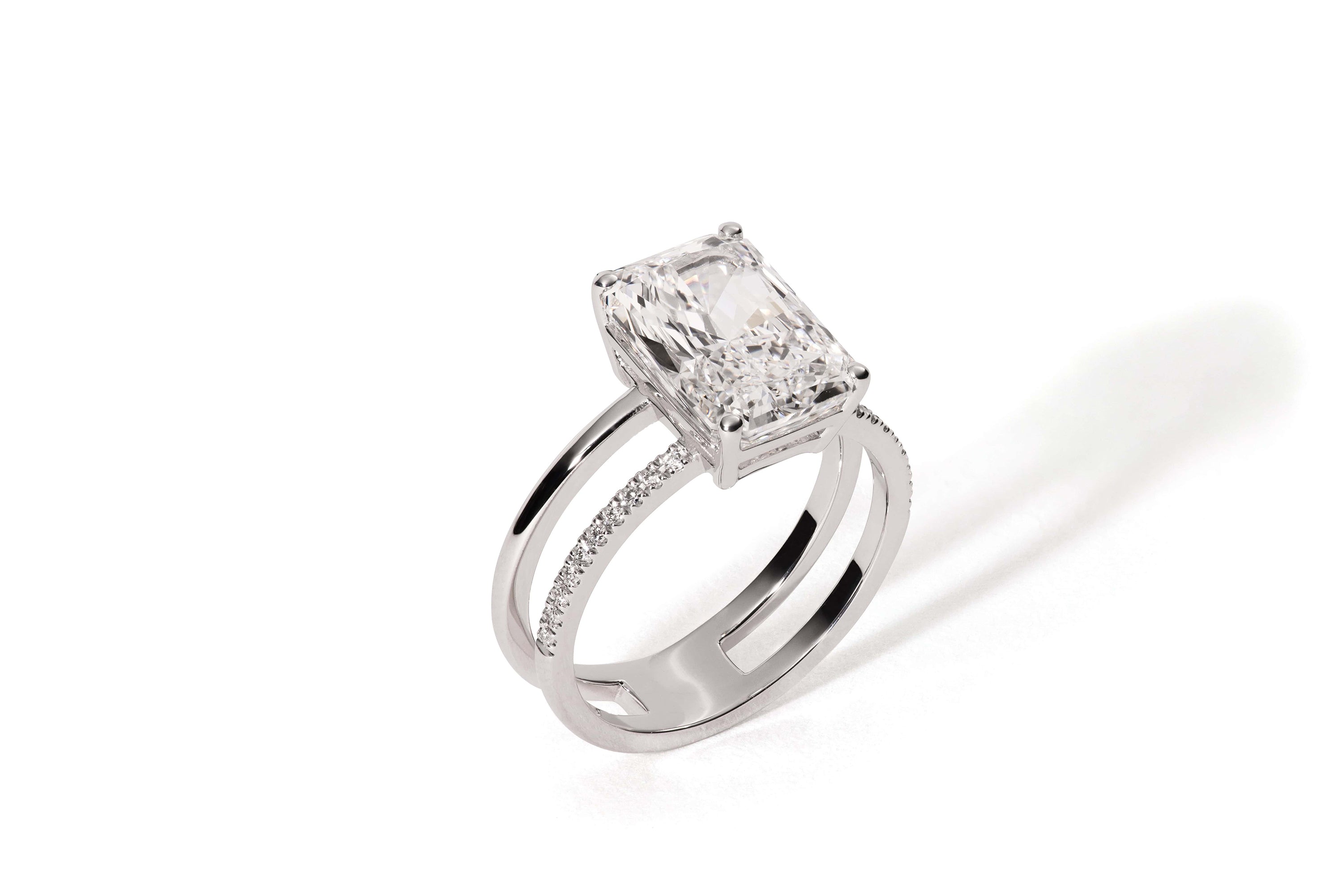 Der APHRODITE WEIßGOLD von Atelier Sofia ist ein Silberring mit einem im Radiantschliff gefertigten, im Labor gezüchteten Diamanten auf einem Doppelband, von denen eines mit kleinen Diamanten verziert ist und das andere schlicht ist und einen sanften Schatten auf Weiß wirft.